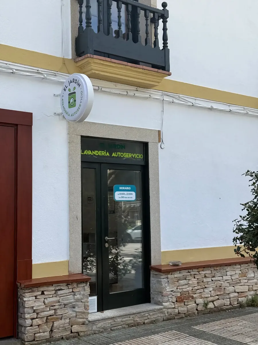 Entrada de la Lavandería El Jardín: puerta negra con el rótulo redondo del logotipo sobre fachada blanca